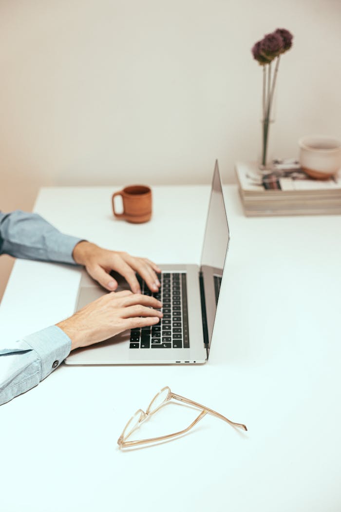 Hands typing on a laptop at a minimalist desk, ideal for remote work or digital nomad lifestyle.